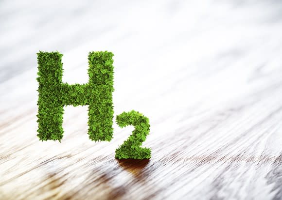 The chemical symbol for hydrogen made of moss hovers over a wooden table.