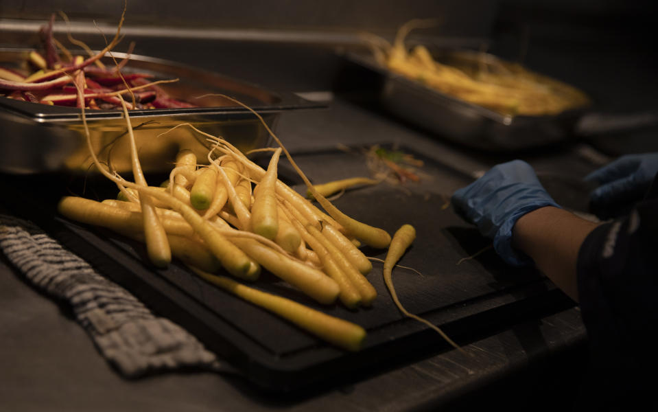 A prep chef peels carrots as she works on nearly 600 take-away orders at Sergio Herman's Le Pristine restaurant in Antwerp, Belgium, Friday, Nov. 6, 2020. Of all the many challenges the pandemic throws up for all kinds of professions, this one has been particularly tough: How to put a three-star chef into a takeout box. (AP Photo/Virginia Mayo)