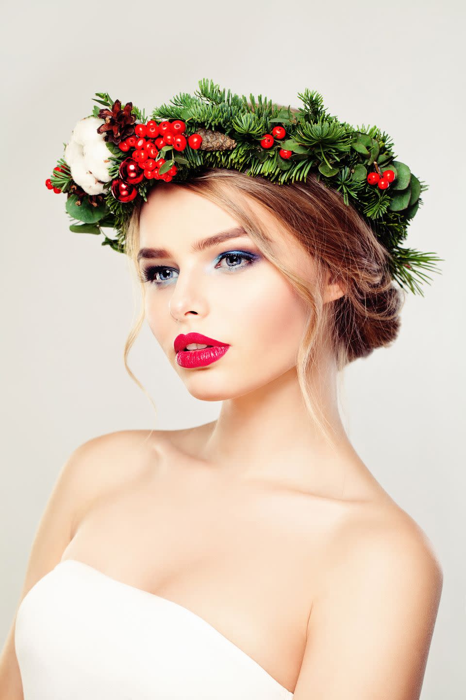 blonde woman wearing christmas evergreen with red berries and christmas balls on head, her hair is in a rolled updo
