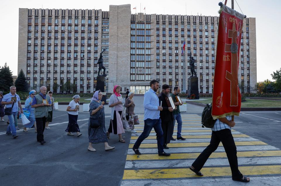 Participants of a religious procession walk past a local government building and the recently unveiled memorial 