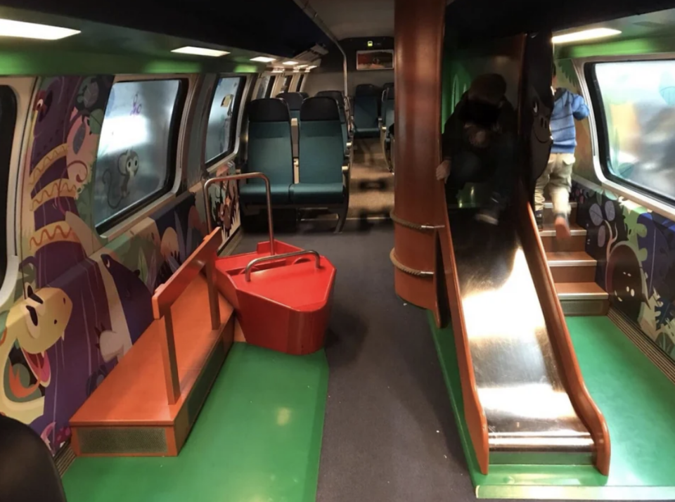 Children's play area inside a train carriage with seats, a slide, and playful decorations