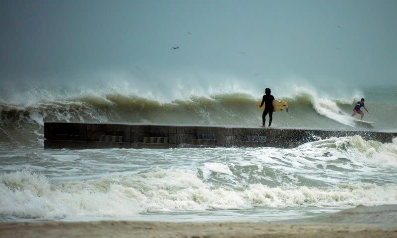 A surfer times the waves before jumping off the jetty into the surf before the arrival of Tropical Storm Eta in Florida
