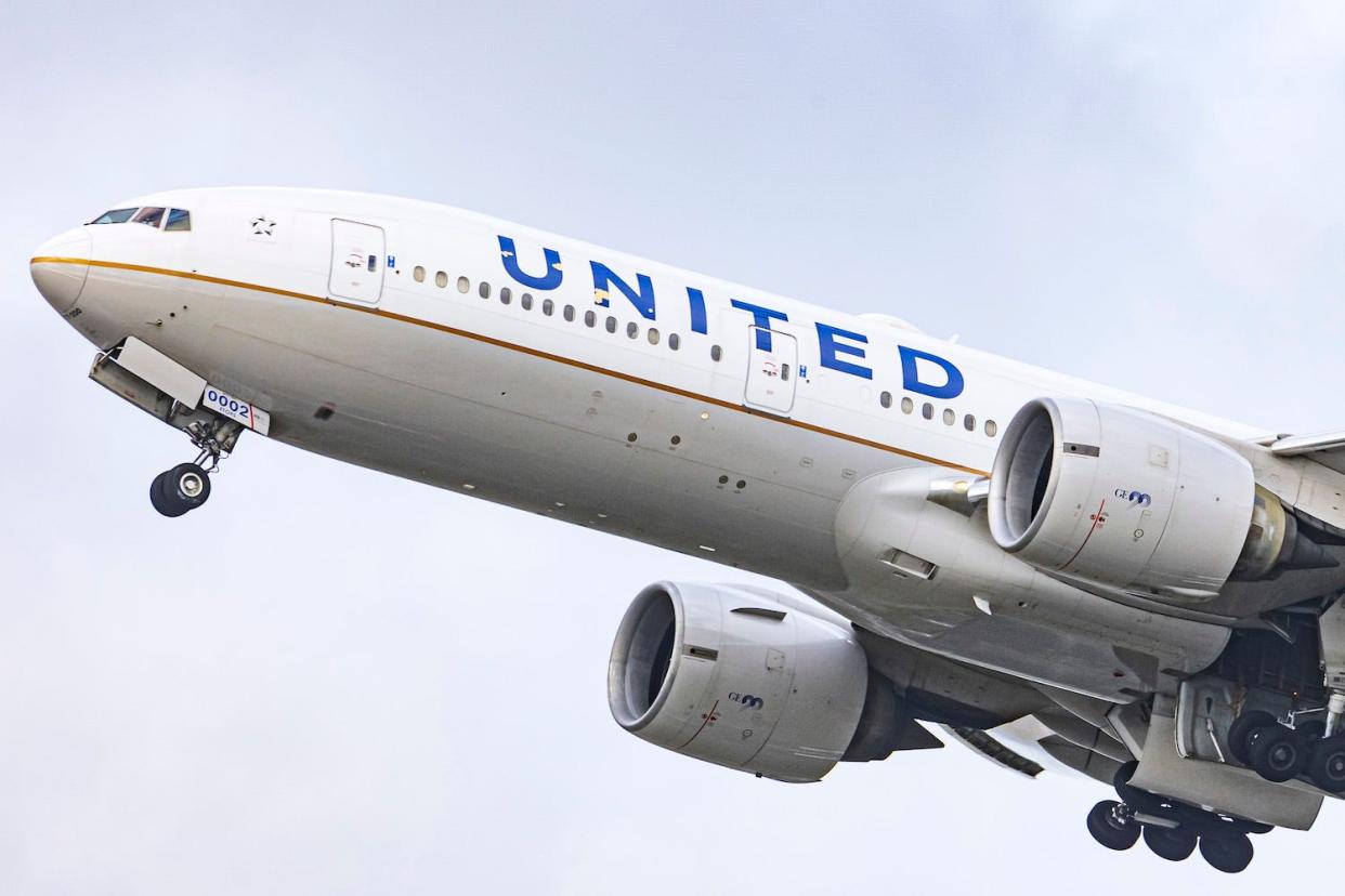 A United Airlines-branded airplane flying with its landing gear down.