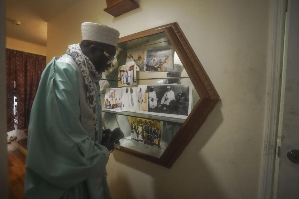 Imam Omar Niass, from Senegal, walks past a photo shelf displaying his father and grandfather, who were also Imams, as he heads to evening prayers at Bronx's Masjid Ansaru-Deen mosque, Friday March 15, 2024, in New York. The mosque, formerly his family home, has served as a refuge and shelter since 2020 for African migrants while seeking asylum in the United States. (AP Photo/Bebeto Matthews)