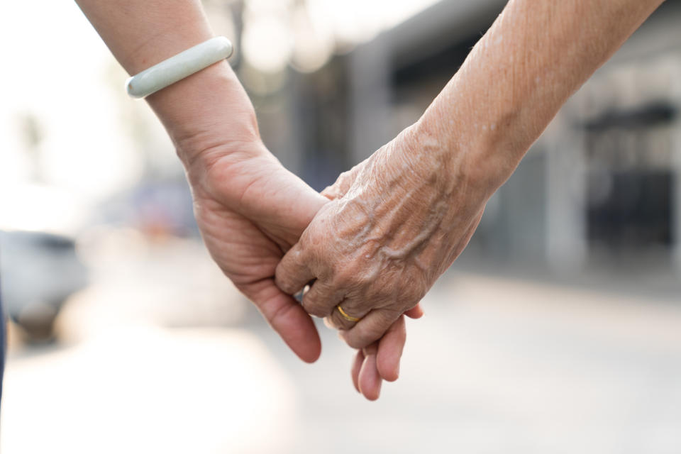 Two people holding hands, one with a jade bracelet and the other wearing a gold ring