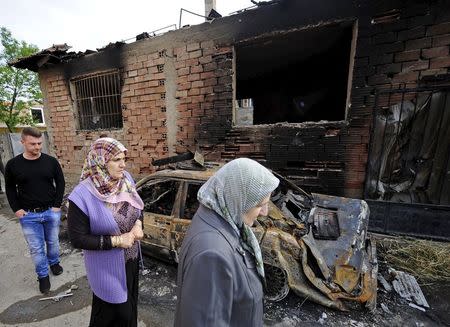 Women walk past a burnt car and damaged houses in Kumanovo, Macedonia May 11, 2015. REUTERS/Ognen Teofilovski