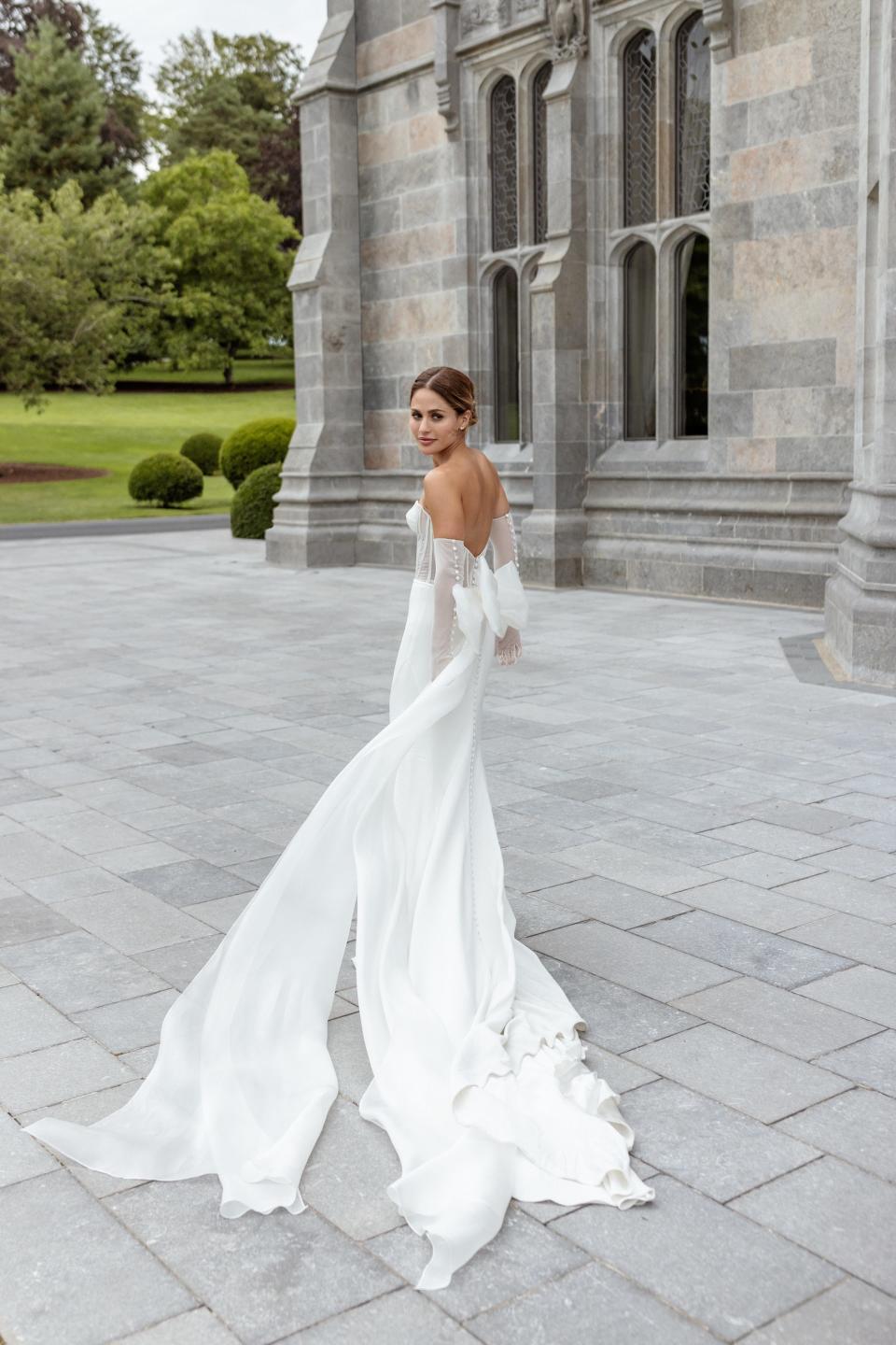 A bride looks over shoulder in front of a stone building.