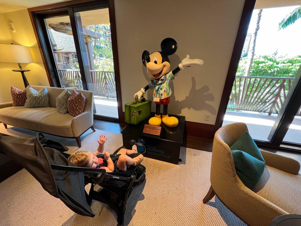 A baby in a stroller looking at a statue of Mickey Mouse dressed for vacation.