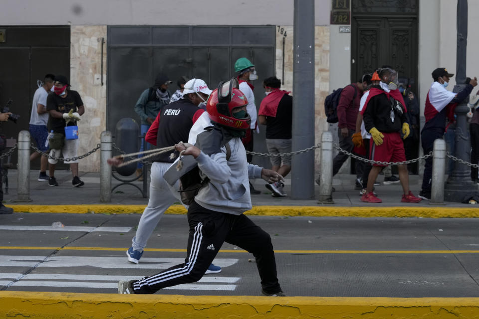 An anti-government protester hurls stones at the police during clashed in Lima, Peru, Tuesday, Jan. 24, 2023. Protesters are seeking the resignation of President Dina Boluarte, the release from prison of ousted President Pedro Castillo, immediate elections and justice for demonstrators killed in clashes with police. (AP Photo/Martin Mejia)