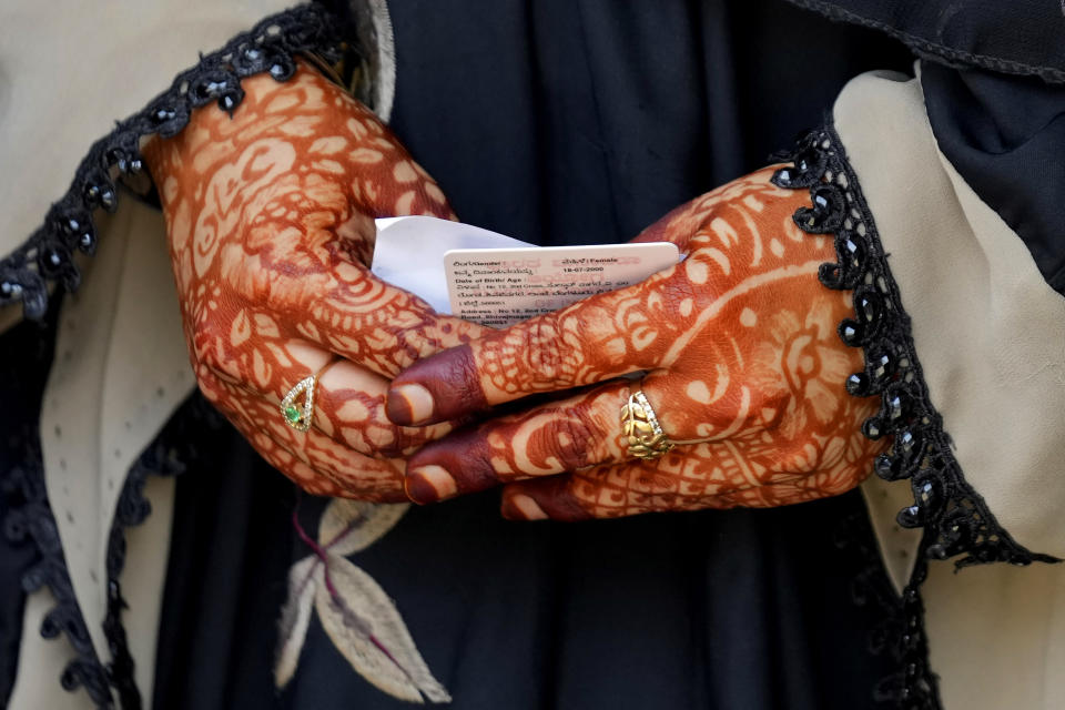 A woman with her hands decorated with henna holds her voter identity card as she waits to cast her vote at a polling station in Bengaluru, India, Wednesday, May 10, 2023. People in the southern Indian state of Karnataka were voting Wednesday in an election where pre-poll surveys showed the opposition Congress party favored over Prime Minister Narendra Modi's governing Hindu nationalist party. (AP Photo/Aijaz Rahi)