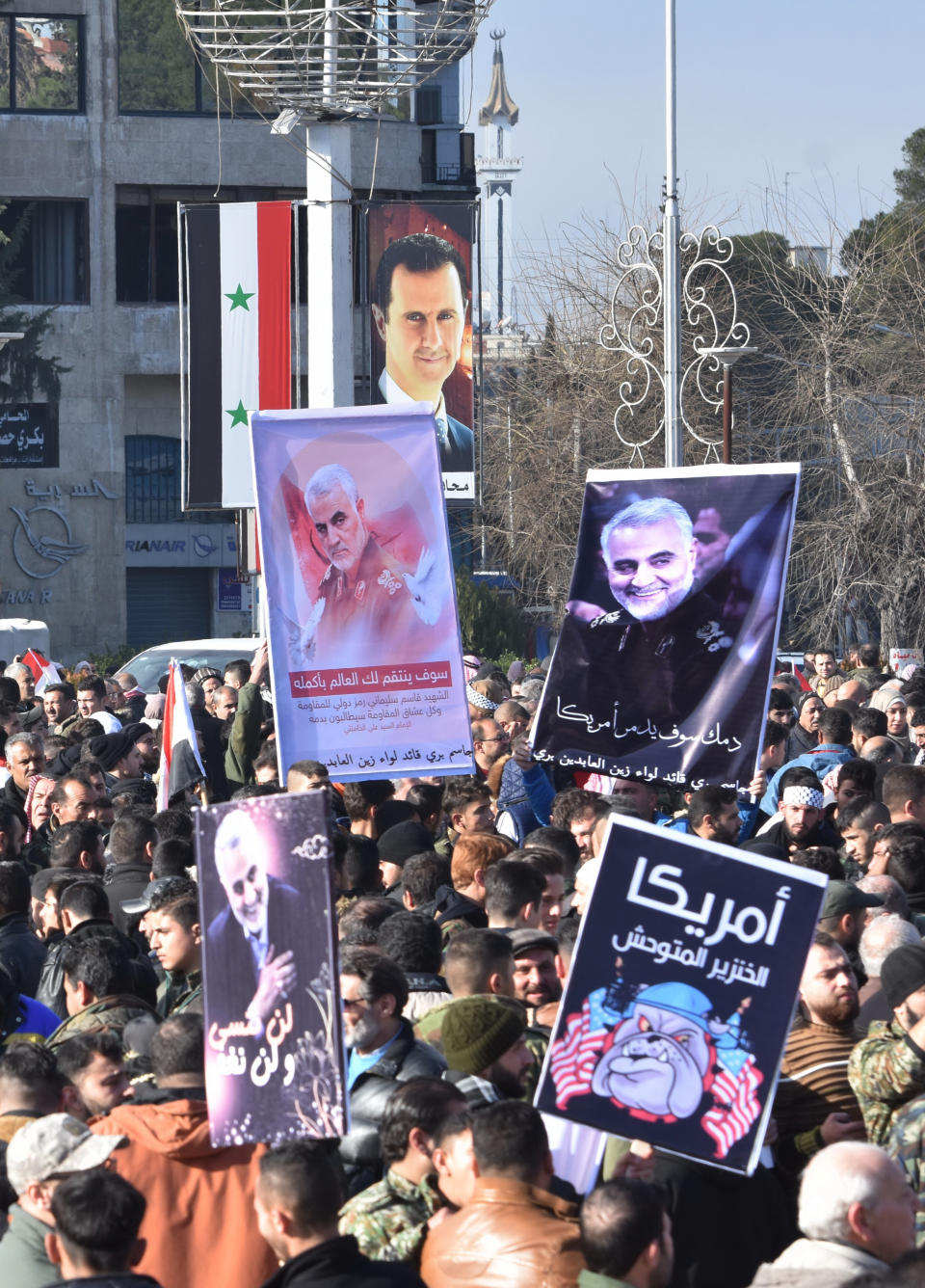 Syrian demonstrators gather under a poster of President Bashar al-Assad (C) in the central Saadallah al-Jabiri square in the northern Syrian city of Aleppo on January 7, 2020, to mourn and condemn the death of Iranian military commander Qasem Soleimani (portrait), and nine others in a US air strike in Baghdad. (Photo by - / AFP) (Photo by -/AFP via Getty Images)