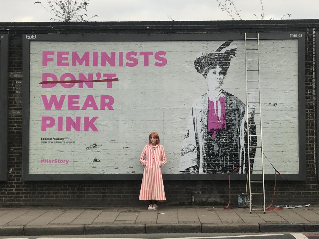 Scarlett Curtis stands in front of an artwork of suffragette leader Emmeline Pankhurst: Feminists Don't Wear Pink / Herstory