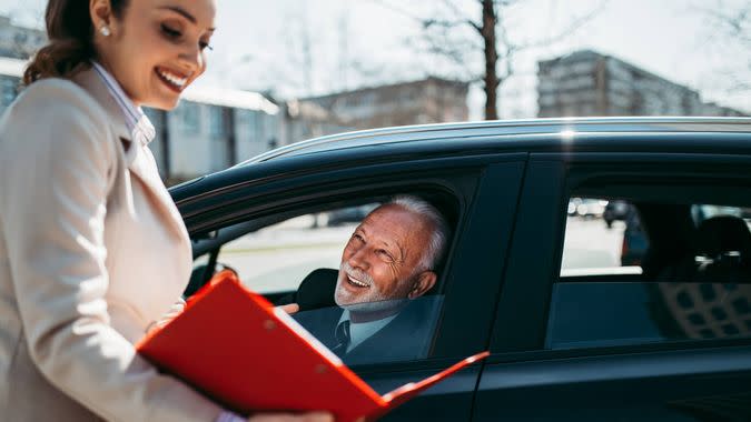 Beautiful young woman sales manager showing car specification to happy senior man buyer.