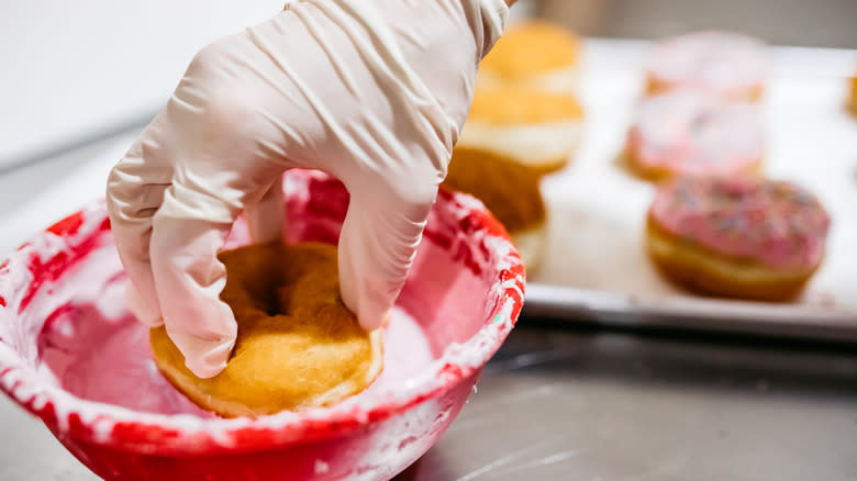 a hand dips a donut into icing