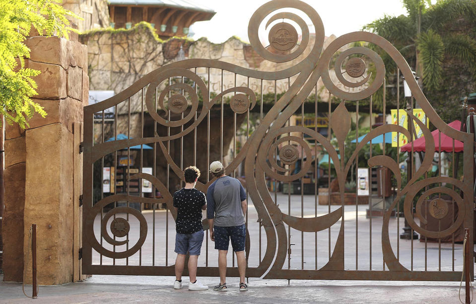 FILE - In this Thursday, May 14, 2020, file photo, guests peer through the closed gate to Universal's Islands of Adventure beside Universal CityWalk, in Orlando, Fla. Universal Orlando is aiming to reopen its theme parks in early June, a resort official said Thursday, May 20, more than two months after the company joined crosstown rival Disney World in closing the gates to stop the spread of the new coronavirus. (Stephen M. Dowell/Orlando Sentinel via AP, File)