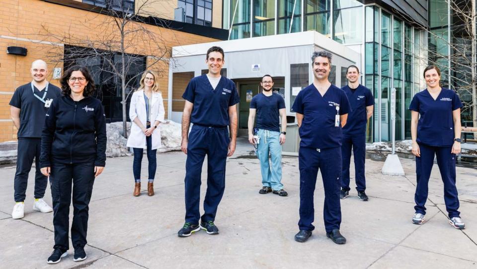 a group of people in medical suits standing in a group outside, some distance apart and smiling