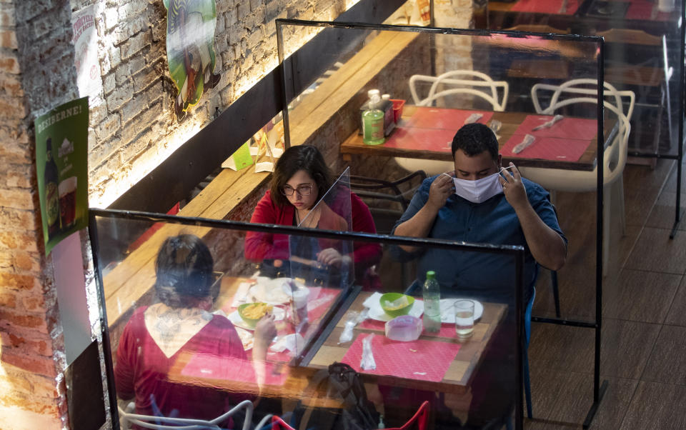 People eat lunch at a restaurant with plastic dividers between tables, as a preventative measure amid the COVID-19 pandemic in Sao Paulo, Brazil, Monday, July 6, 2020. Bars, restaurants and beauty salons were allowed to re-open Monday after over three months of quarantine, but are required to observe preventative measures and reduced operating hours only during the day. (AP Photo/Andre Penner)