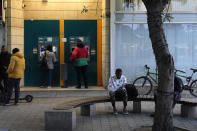 A migrant sits on a bench as others use an ATM machine at Elepfhteria, Liberty Square in divided capital Nicosia, Cyprus, Saturday, Jan. 28, 2023. Cypriots are voting Sunday for a new president who they’ll expect to decisively steer the small island nation through shifting geopolitical sands and uncertain economic times that have become people's overriding concern, eclipsing stalemated efforts to remedy the country’s ethnic division. (AP Photo/Petros Karadjias)