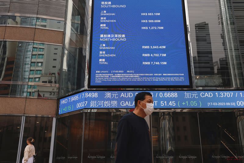 People walk past a screen displaying the Hang Seng Index at Central district, in Hong Kong