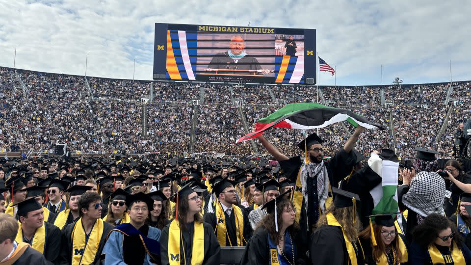A protester holds a Palestinian flag as the Secretary of the Navy delivered remarks at the University of Michigan’s 2024 spring commencement. - CNN