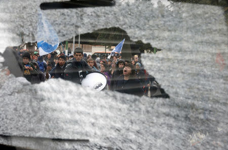 Demonstrators are seen through a broken glass of a car as they shout slogans during an unauthorized march called by secondary students to protest against government education reforms in Valparaiso, Chile, May 26, 2016. REUTERS/Rodrigo Garrido