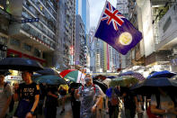 A protester waves a Hong Kong colonial-era flag as others march along a street in Hong Kong, Sunday, Aug. 18, 2019. Heavy rain fell on tens of thousands of umbrella-toting protesters Sunday as they marched from a packed park and filled a major road in Hong Kong, where mass pro-democracy demonstrations have become a regular weekend activity this summer. (AP Photo/Vincent Yu)