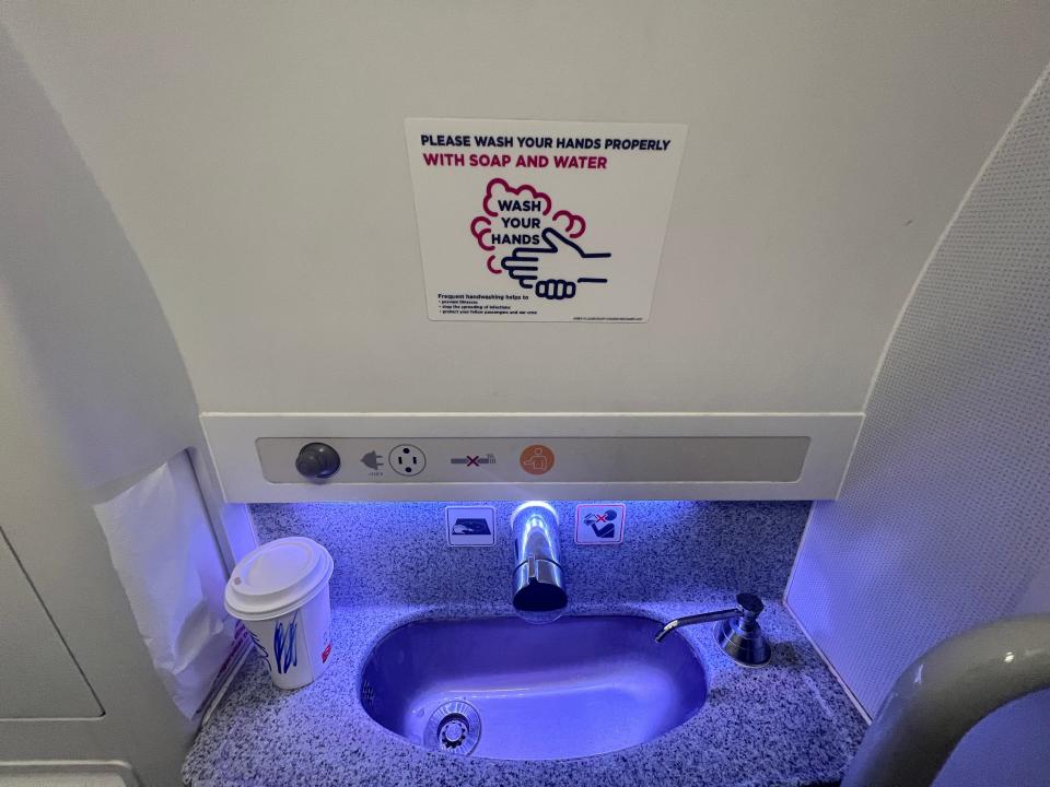 The bathroom on board a Wizz Air Airbus A320neo has a blue-purple light and a coffee cup next to the sink