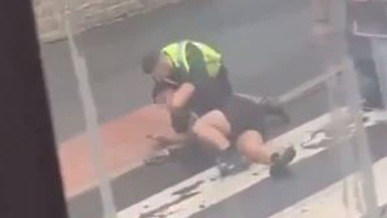 An officer grapples with the man and appears to say 'chill out or I'll choke you out'