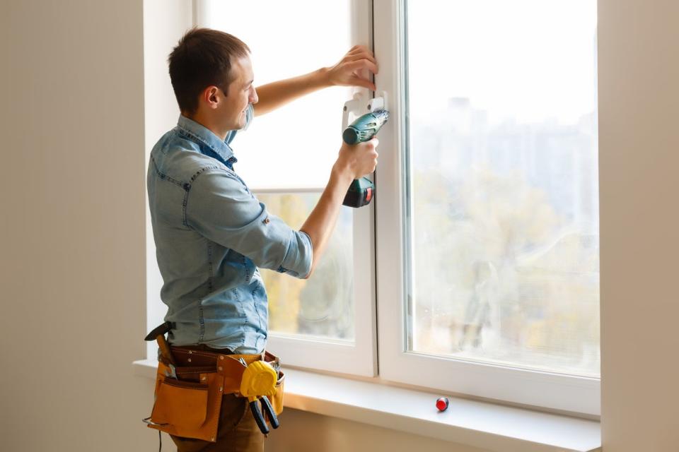 Man wearing a tool belt and holding a drill, installing a window.
