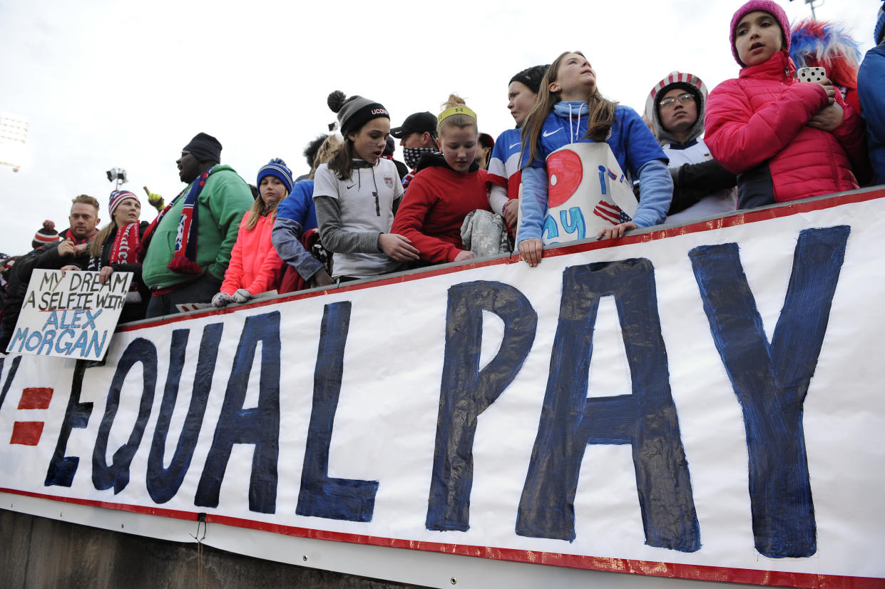 FILE - In this April 6, 2016, file photo, fans stand behind a large sign for equal pay for the women's soccer team during an international friendly soccer match between the United States and Colombia at Pratt & Whitney Stadium at Rentschler Field in East Hartford, Conn. The World Economic Forum's annual Global Gender Gap Report released on Oct. 25, 2016, found that the global gender pay gap will not be closed for another 170 years if current trends continue. (AP Photo/Jessica Hill, File)