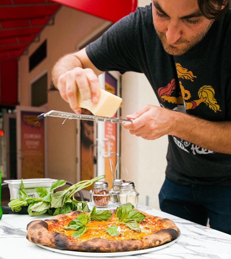 David Foulquier, co-owner of Eleventh Street Pizza, grates Parmesan over a Classic Cheese pizza made with sourdough crust at the new restaurant in Kendall.