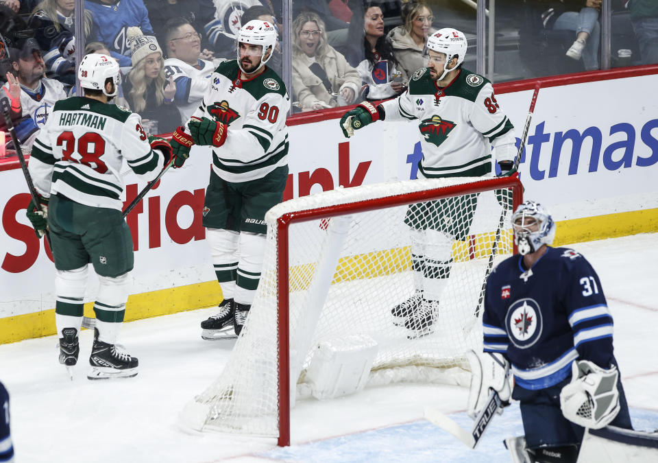 Minnesota Wild's Ryan Hartman (38), Marcus Johansson (90) and Frederick Gaudreau (89) celebrate Hartman's goal against Winnipeg Jets goaltender Connor Hellebuyck (37) during the second period of an NHL hockey game, Saturday, Dec. 30, 2023 in Winnipeg, Manitoba. (John Woods/The Canadian Press via AP)