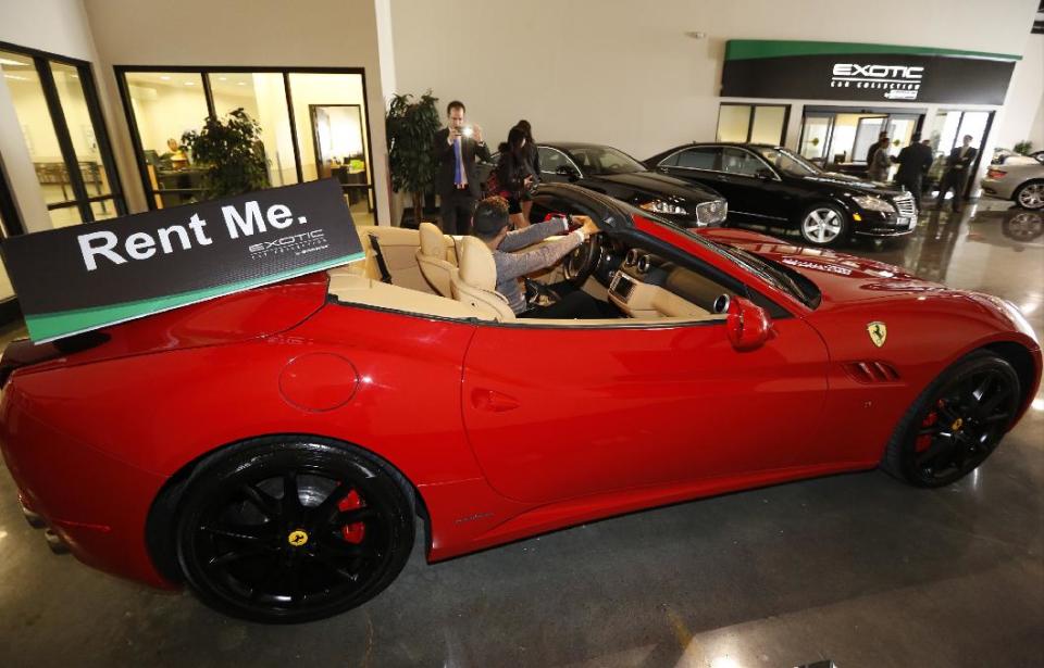 In this Wednesday, March, 26, 2014 photo, customer Luis Montelongo, from Monterrey, Mexico has his photo taken on a 2014 Ferrari California displayed for rent at the Enterprise Exotic Car Collection showroom near Los Angeles International Airport. (AP Photo/Damian Dovarganes)