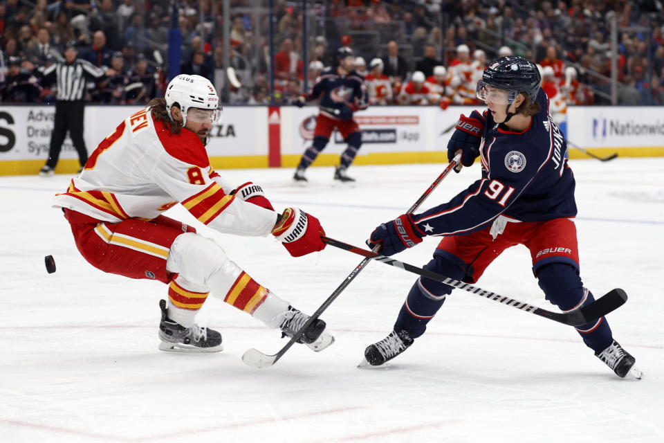 Columbus Blue Jackets forward Kent Johnson, right, passes the puck in front of Calgary Flames defenseman Chris Tanev during the second period of an NHL hockey game in Columbus, Ohio, Friday, Oct. 20, 2023. (AP Photo/Paul Vernon)