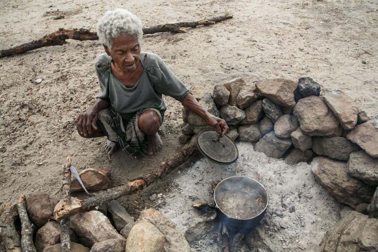 Mrs. Behora, about 80, squats in the ground to cook food in a pot at her house in the village of Fenoaivo.