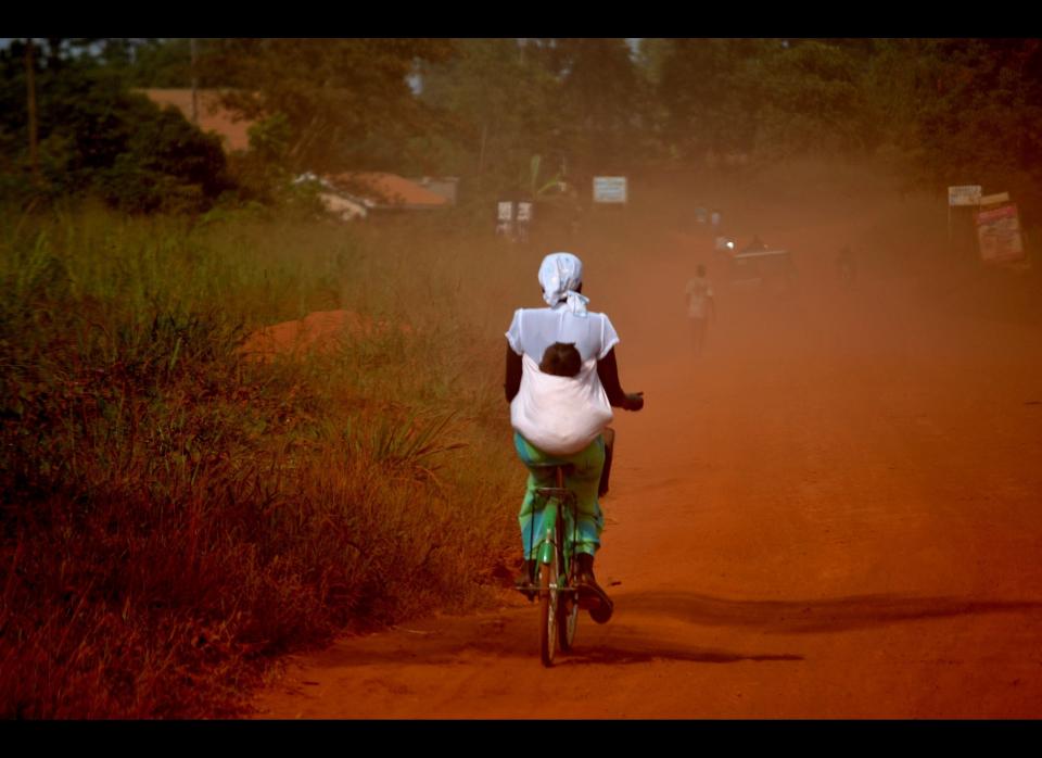 A woman, carrying her baby on her back, rides her bicycle outside the town of Gulu, in northern Uganda.   According to the 2011 Demographic and Health Survey, 65% of married women in northern Uganda, have experienced a form of violence from their partner; one third of married women have also reported sexual violence. It was raised that men over drink and spend little time in economically productive activities, resulting into several forms of domestic violence.  