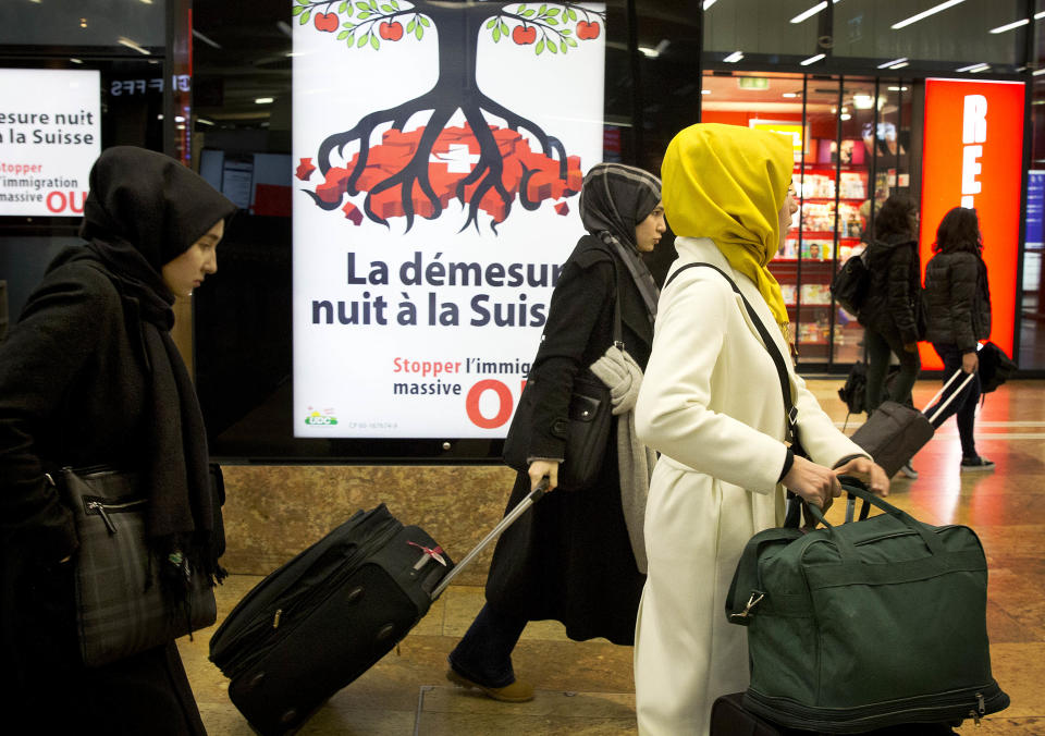 FILE - In this Feb. 7 2014 file picture women covered in veils pass by an election poster from the nationalist Swiss People’s Party, demanding a stop for immigration to Switzerland and reading: excess harms Switzerland , at the train station in Geneva, Switzerland, Swiss voters are being asked to decide on a proposal Sunday Feb. 9, 2014 to cap immigration to the Alpine republic, a long-standing demand of Switzerland’s most powerful party. (AP Photo/Anja Niedringhaus,File)