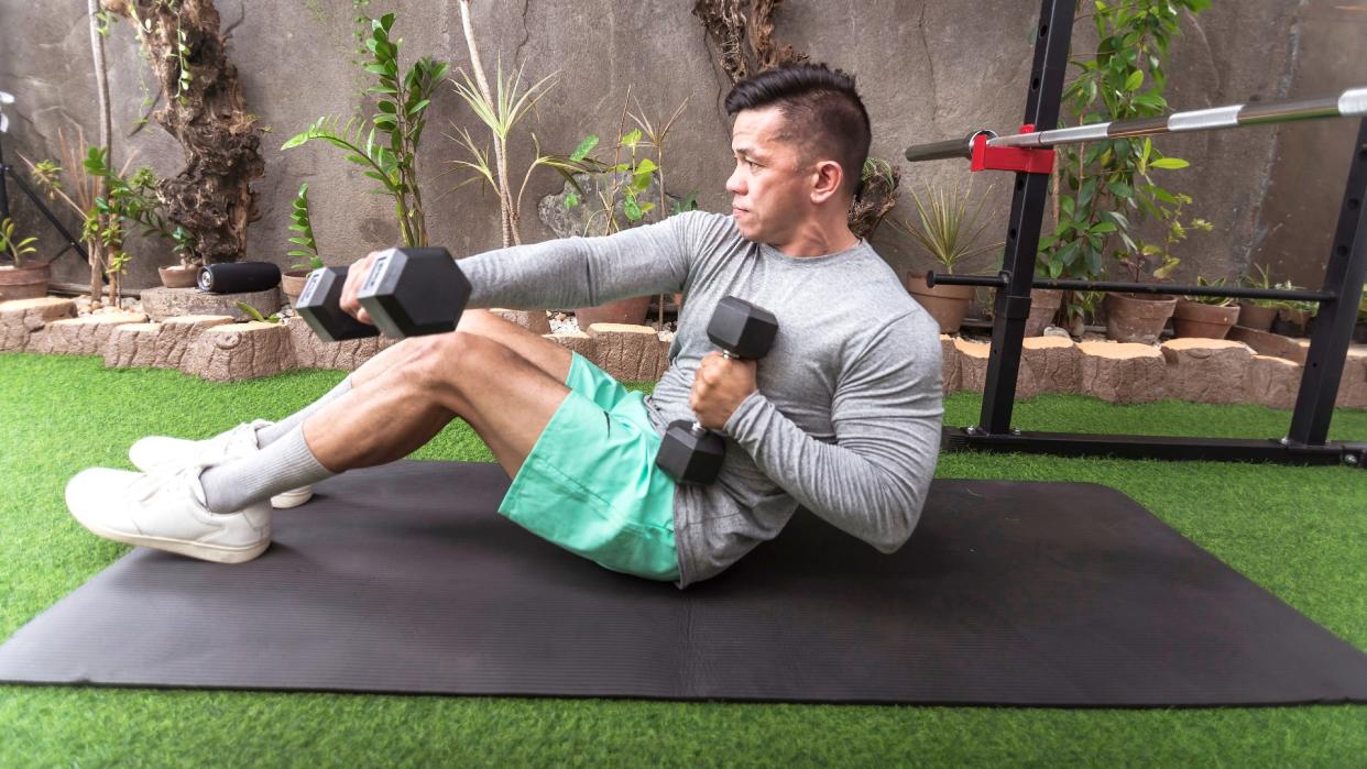  Man on exercise mat performing sit-up punches with right arm forward holding a pair of dumbbells 