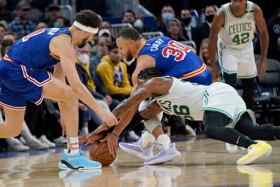 Boston Celtics' Marcus Smart, bottom, reaches for the ball against Golden State Warriors' Stephen Curry and Klay Thompson in San Francisco, Wednesday, March 16, 2022. Curry left the game after this play.