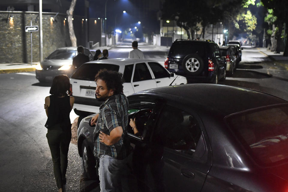 People stand close to their vehicles as they wait in line to fill up their vehicles with gasoline in Caracas, Venezuela, Saturday, April 11, 2020. Lines at gas stations around the country's capital looked getting longer Saturday. (AP Photo/Matias Delacroix)