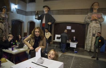 A child deposits her mother's ballot at a polling station in a school in front of Catalan "Gegants", or giant figures, while voting in a symbolic independence vote in Barcelona, November 9, 2014. REUTERS/Paul Hanna