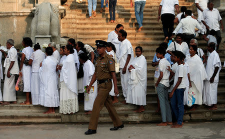 A police officer walks past worshipers at the Kelaniya Buddhist temple during Vesak Day, commemorating the birth, enlightenment and death of Buddha, in Colombo, Sri Lanka May 18, 2019. REUTERS/Dinuka Liyanawatte