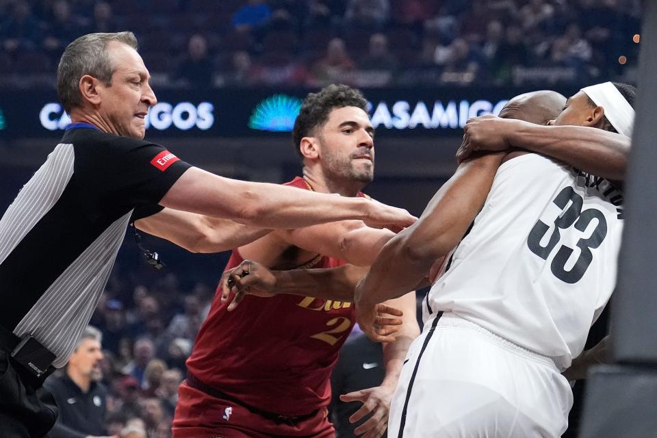 Cleveland Cavaliers forward Georges Niang, center, and Brooklyn Nets center Nic Claxton (33) are separated by referee J.T. Orr, left, and referee Courtney Kirkland (61), second from right, in the first half of an NBA basketball game, Sunday, March 10, 2024, in Cleveland. (AP Photo/Sue Ogrocki)