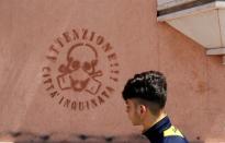 A man walks past a graffiti reading "Attention, polluted city" in the Tamburi district, in Taranto, southern Italy April 27, 2018. Picture taken April 27, 2018. REUTERS/Tony Gentile