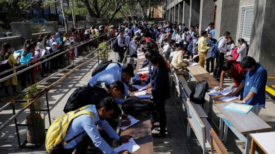 Job seekers fill up forms as others line up for registration during a job fair in Chinchwad