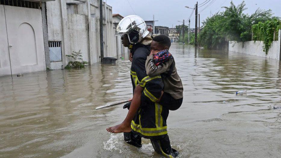 A firefighter carries a child as he walks in flood water in Cocody Angre in Abidjan on June 14, 2024 after torrential rains. Flooding and landslips have killed five people in Abidjan, Ivory Coast's biggest city, after heavy downpours, the fire service said on Friday. Roads were cut off as the rains fell on Thursday afternoon in most areas of the city with a population of six million.