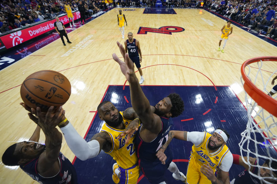 LeBron James, centro, de los Lakers de Los Ángeles, se alza para intentar un tiro entre De'Anthony Melton, izquierda, y Joel Embiid, de los 76ers de Filadelfia, durante la segunda mitad del juego de baloncesto de la NBA, el lunes 27 de noviembre de 2023, en Filadelfia. (AP Foto/Matt Slocum)