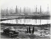 'People chat by a car parked by a field of oil rigs on Signal Hill, Los Angeles, California.' (B. Anthony Stewart /The National Geographic/Christie’s Images) <br> <br> <a href="https://www.christies.com/services/publications/browse-ecatalogues.aspx" rel="nofollow noopener" target="_blank" data-ylk="slk:Click here to see the full collection at Christie's;elm:context_link;itc:0;sec:content-canvas" class="link ">Click here to see the full collection at Christie's</a>