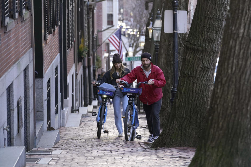 Passers-by walk their bikes up a hill in a residential area near the Statehouse on Beacon Hill, Monday, Feb. 13, 2023, in Boston. For much of the Eastern United States, the winter of 2023 has been a bust. Snow totals are far below average from Boston to Philadelphia in 2023 and warmer temperatures have often resulted in more spring-like days than blizzard-like conditions. (AP Photo/Steven Senne)