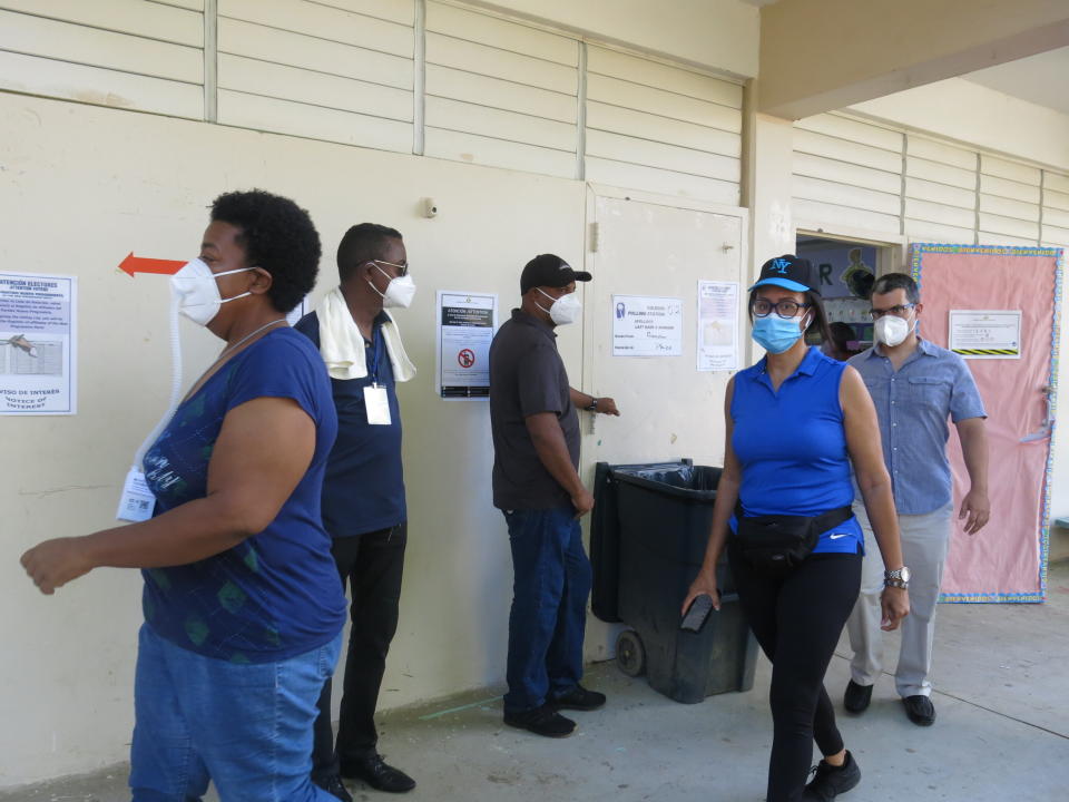 Voters leave a classroom with the required face masks after casting their ballots as volunteers look on in Loíza, Puerto Rico, Sunday, Aug. 16, 2020. Thousands of Puerto Ricans on Sunday got a second chance to vote for the first time, a week after delayed and missing ballots marred the original primaries in a blow to the U.S. territory’s democracy. (AP Photo/Dánica Coto) (AP Photo/Dánica Coto)